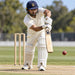 CA Gold 20K white cricket batting leg guards worn by a batter playing a shot in a cricket match