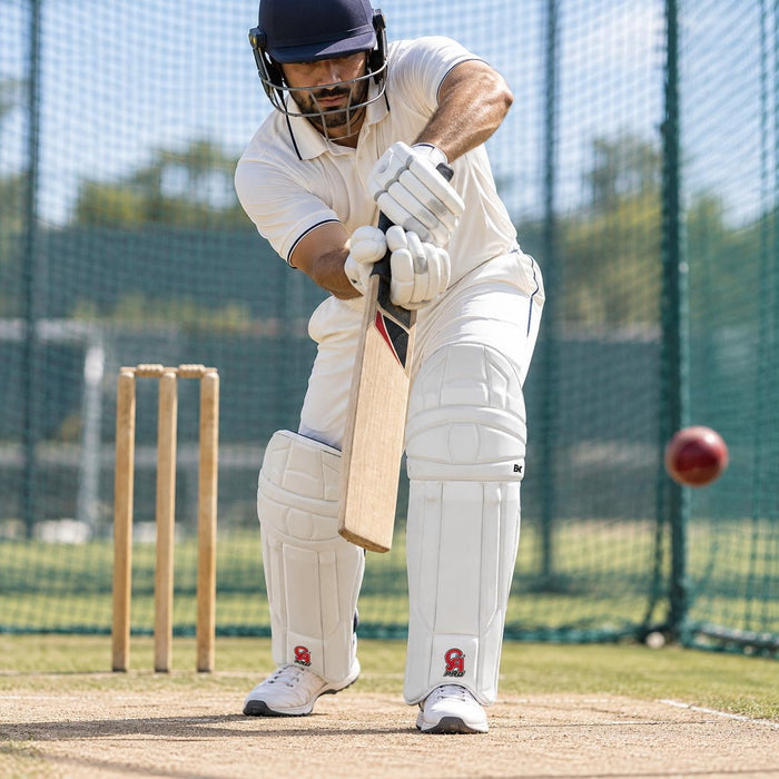 CA Pro 8K white cricket batting leg guards with red CA PRO logo worn by batter playing a defensive shot in nets