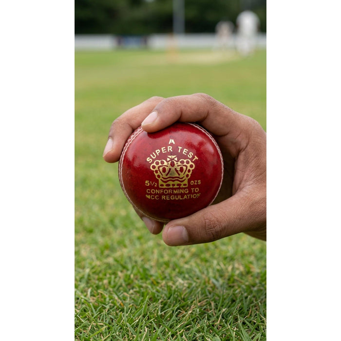 CA Super Test red leather cricket ball held in a hand on a cricket ground