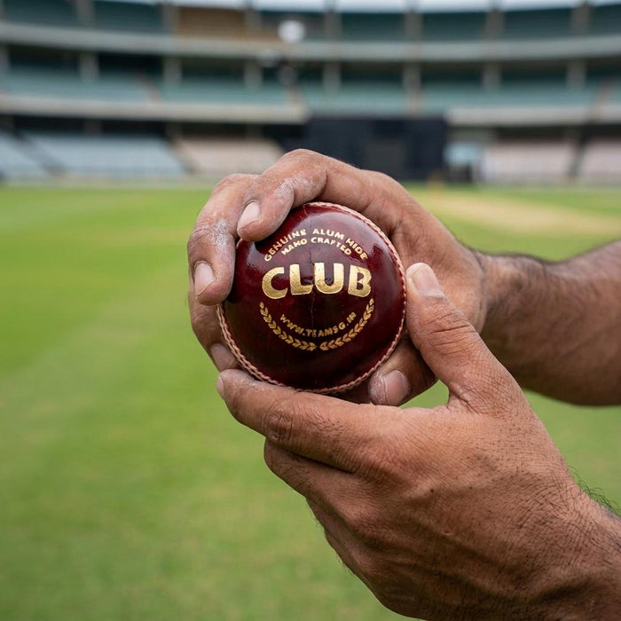 Red SG Club Youth cricket ball held in hands with wrists and forearms visible