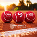 Three red SG Club Heavy tennis cricket balls on a pitch at sunset