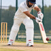 Cricketer wearing white MRF batting leg guards while playing a defensive shot in practice nets