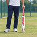 Adult holding the MRF Jumbo white plastic cricket bat with pink grip beside a practice net