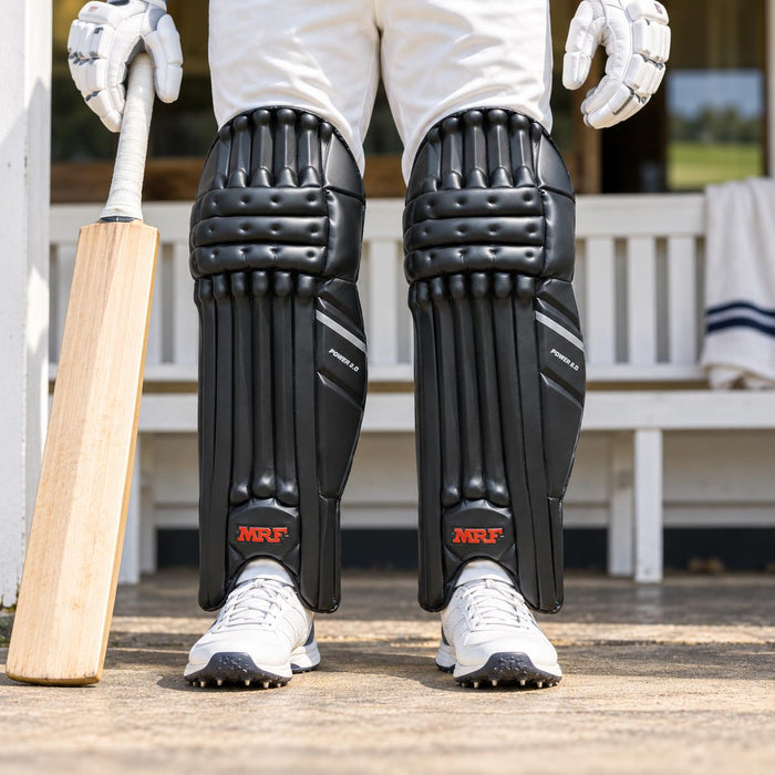 MRF Power 2.0 black batting leg guards worn by a mens cricketer in a front detail view