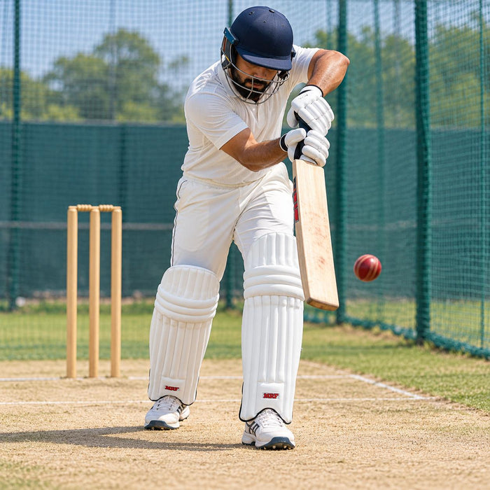 Adult cricketer wearing white MRF Prodigy batting leg guards during a defensive shot in cricket nets