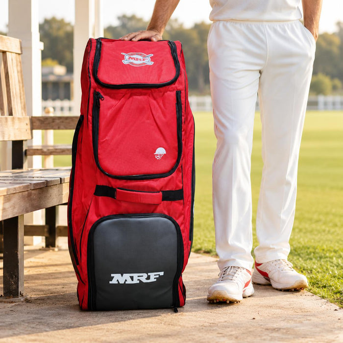 MRF Genius Emperor red and grey kit bag beside a cricketer at the pavilion