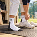 SG Club white and black cricket socks worn while putting on cricket shoes beside the nets